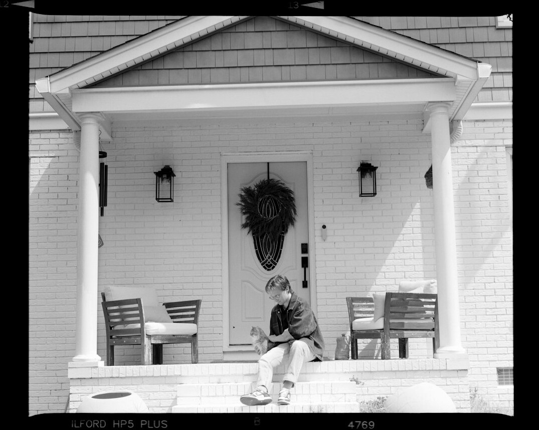 Photographer kneeling to photograph an elderly man on a porch